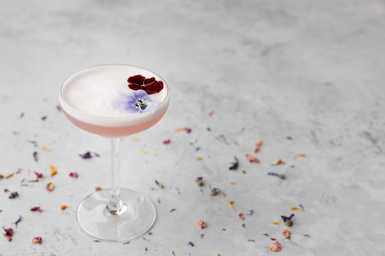 A pink cocktail with edible flowers and scattered petals