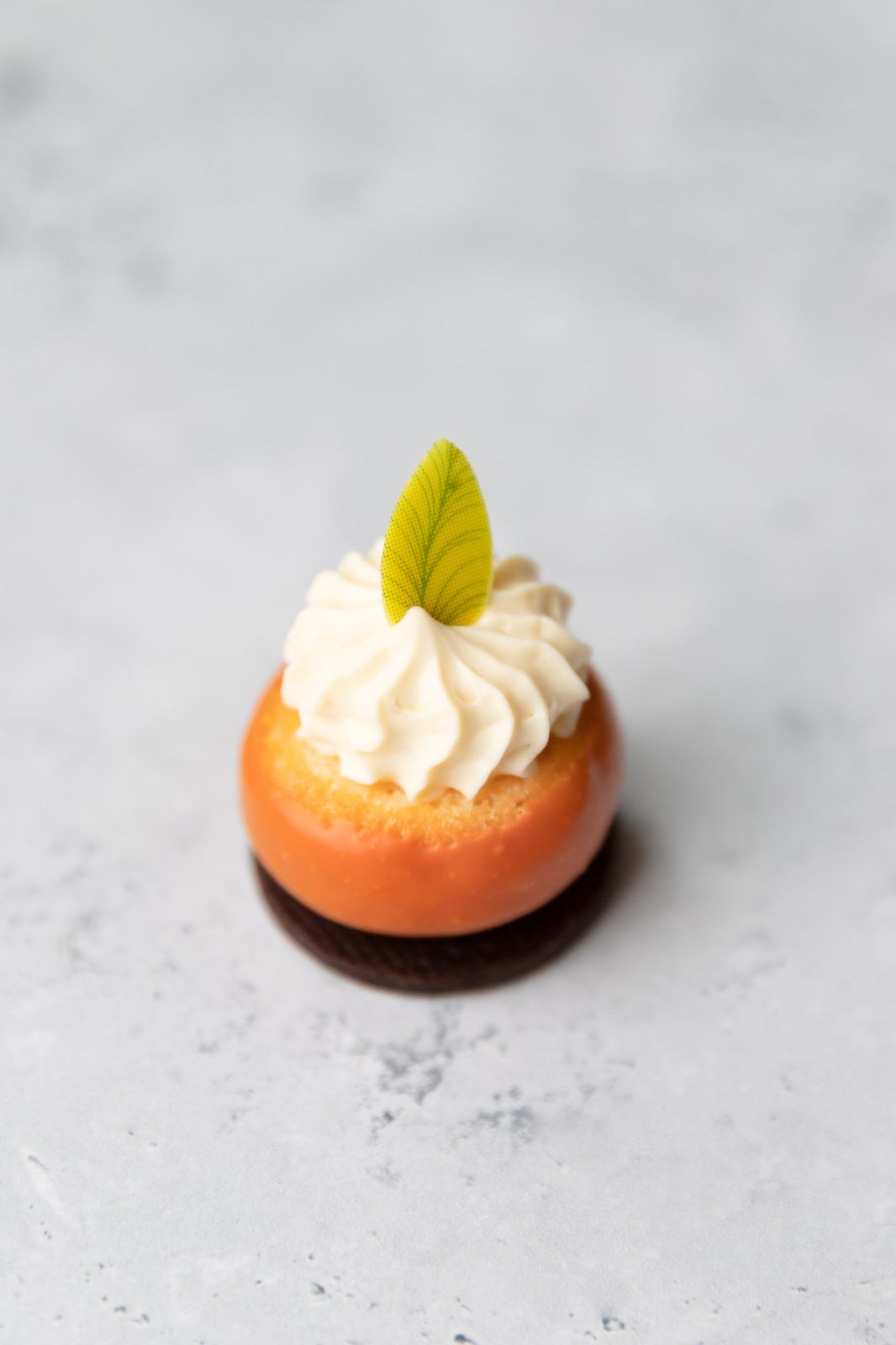 A single orange cake topped with cream and a sugar leaf