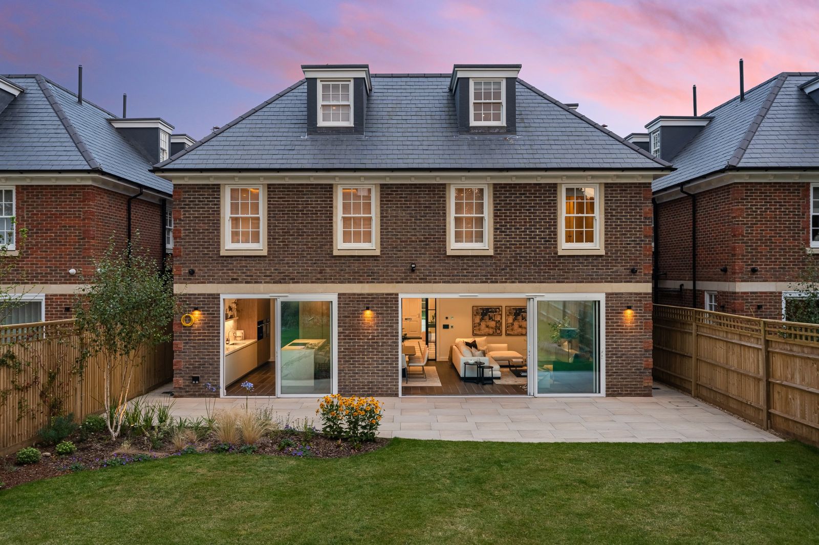 The back of a house at dusk with a tidy lawn and patio