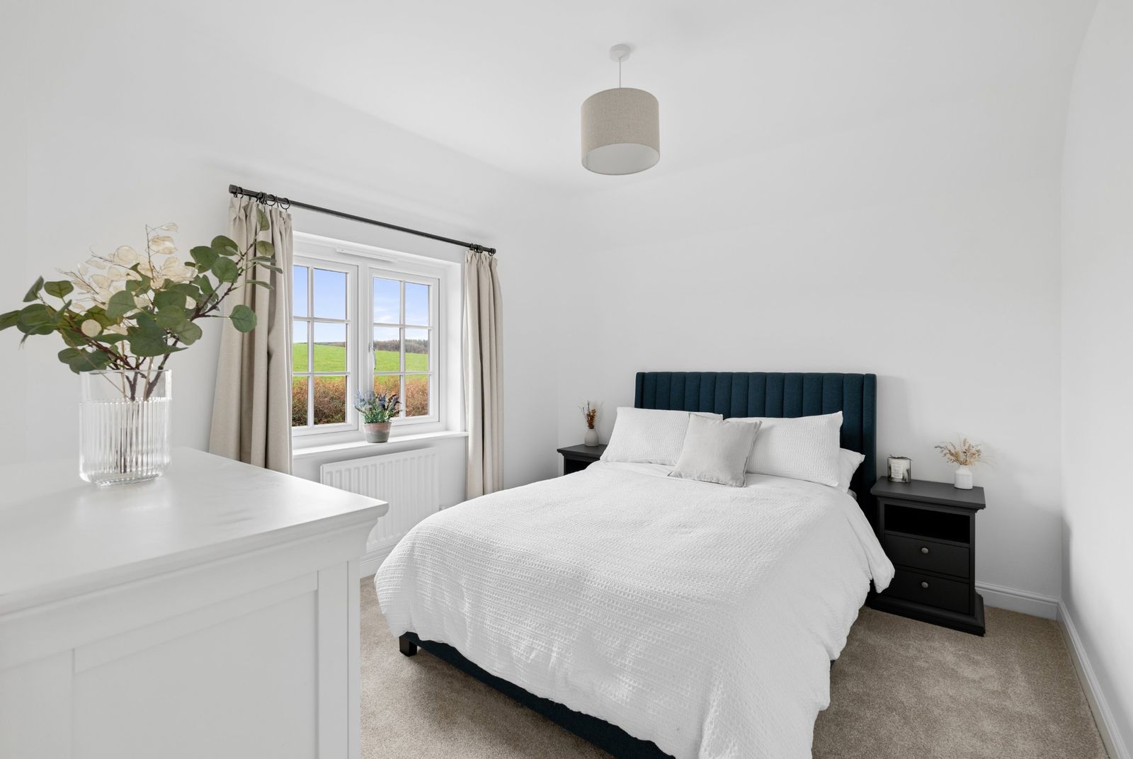 A bedroom with a navy headboard and countryside view
