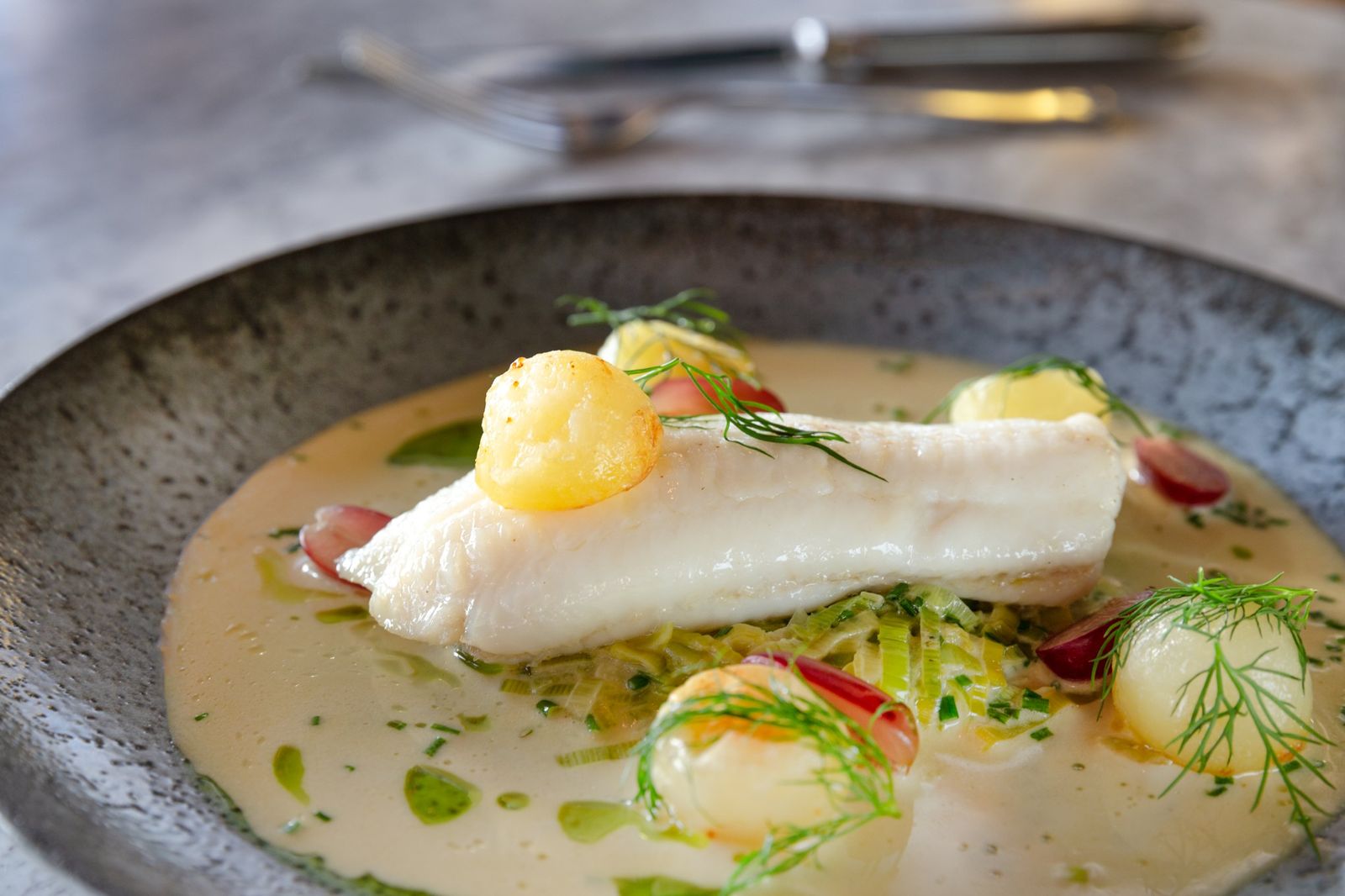 Poached white fish with leeks and grapes, close up