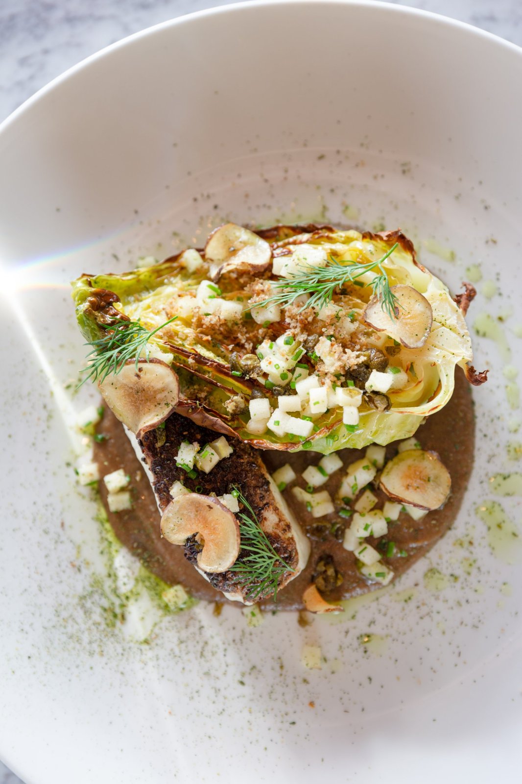 Roasted hispi cabbage with apple, capers and dill on a white plate