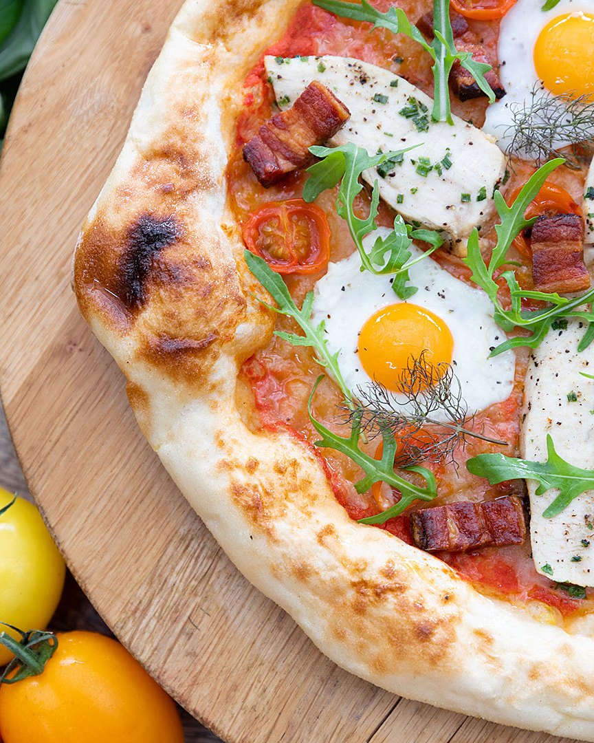 A wood-fired breakfast pizza with fried eggs and bacon