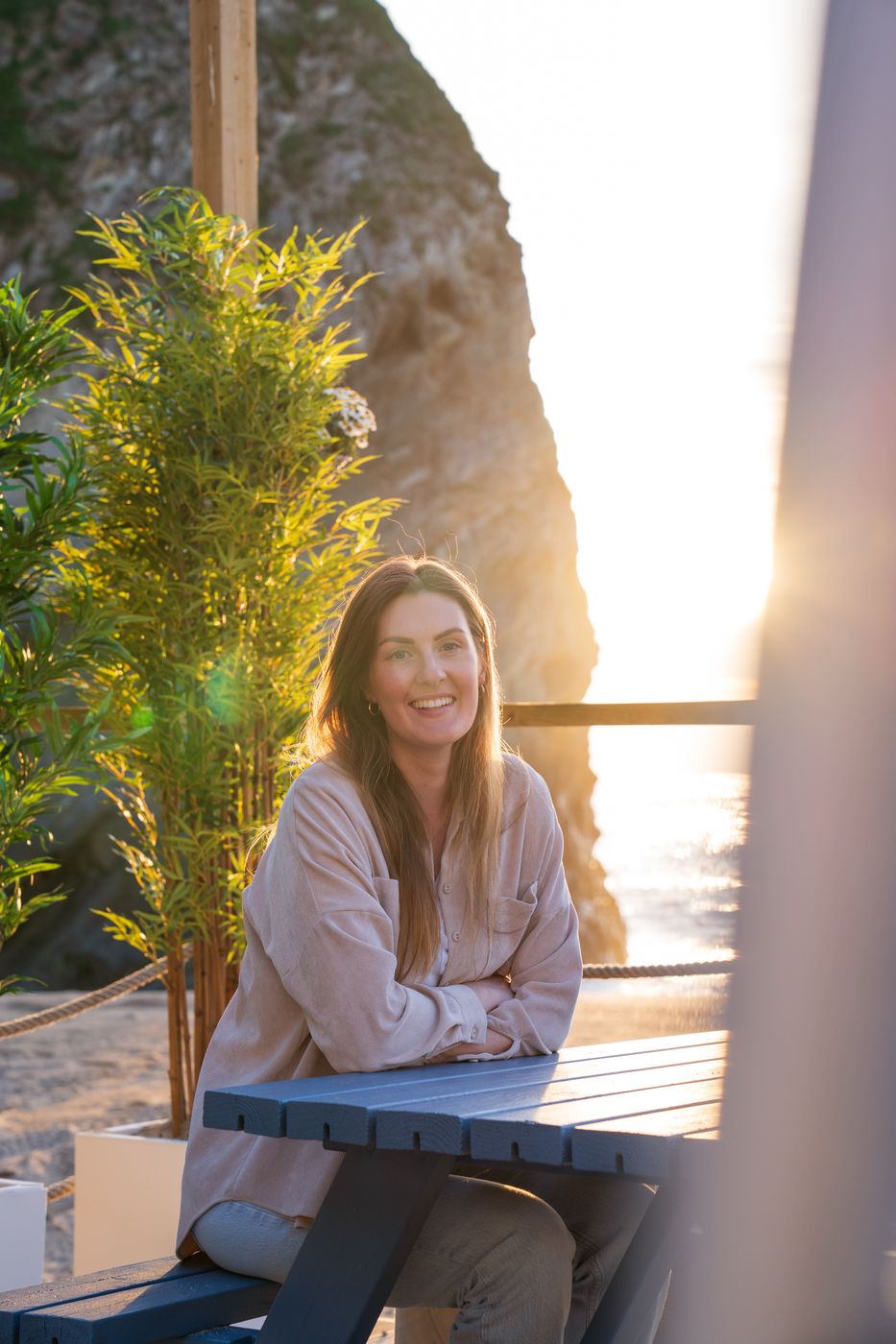 Kelly of Shoreline Bay Studios sitting at a table by the beach at sunset