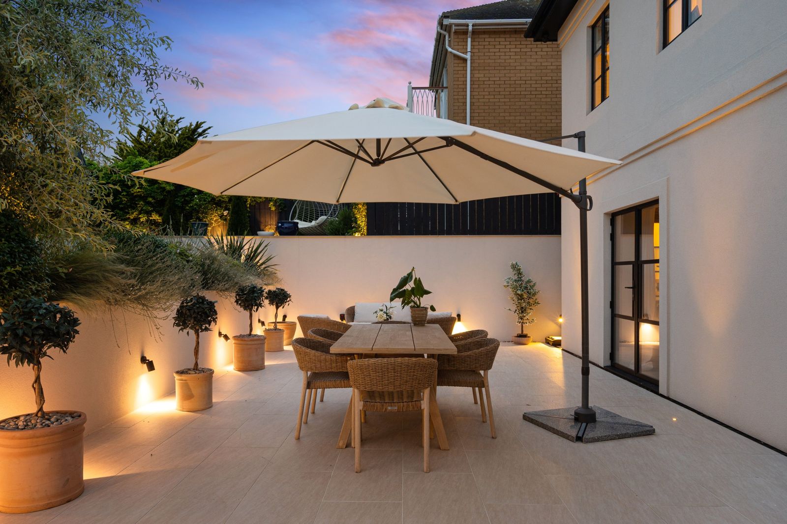 The terrace at dusk with a dining table under a large parasol