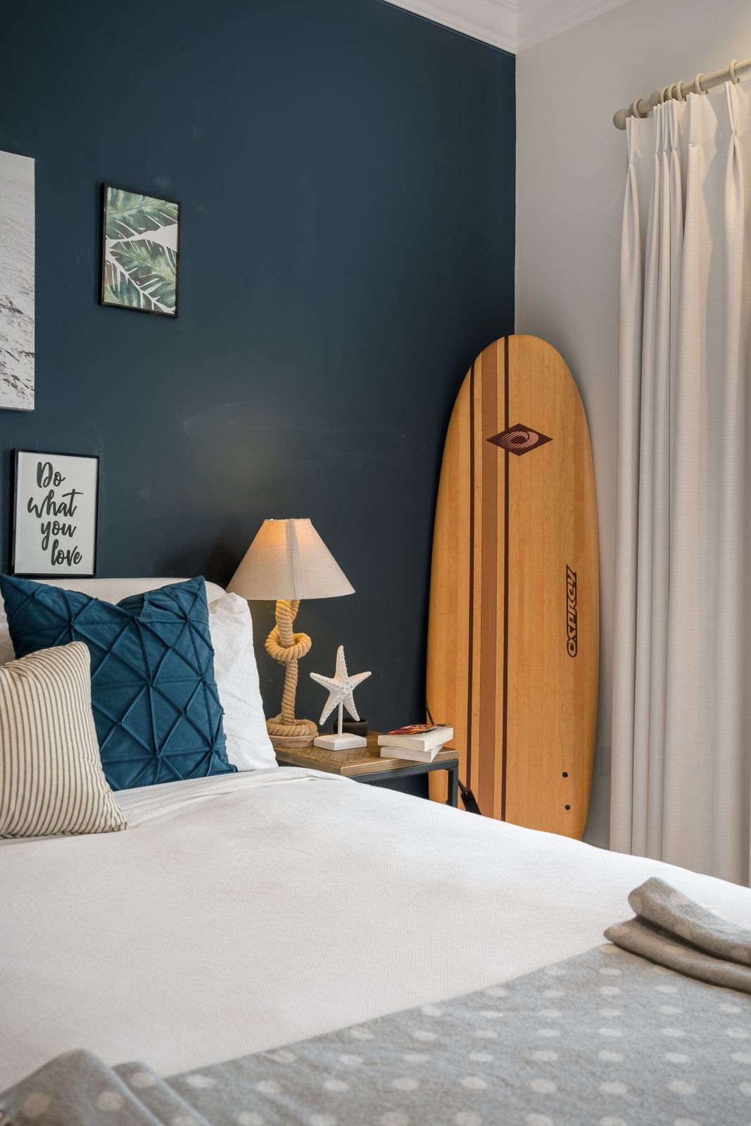 A surfboard beside the bed in the navy bedroom