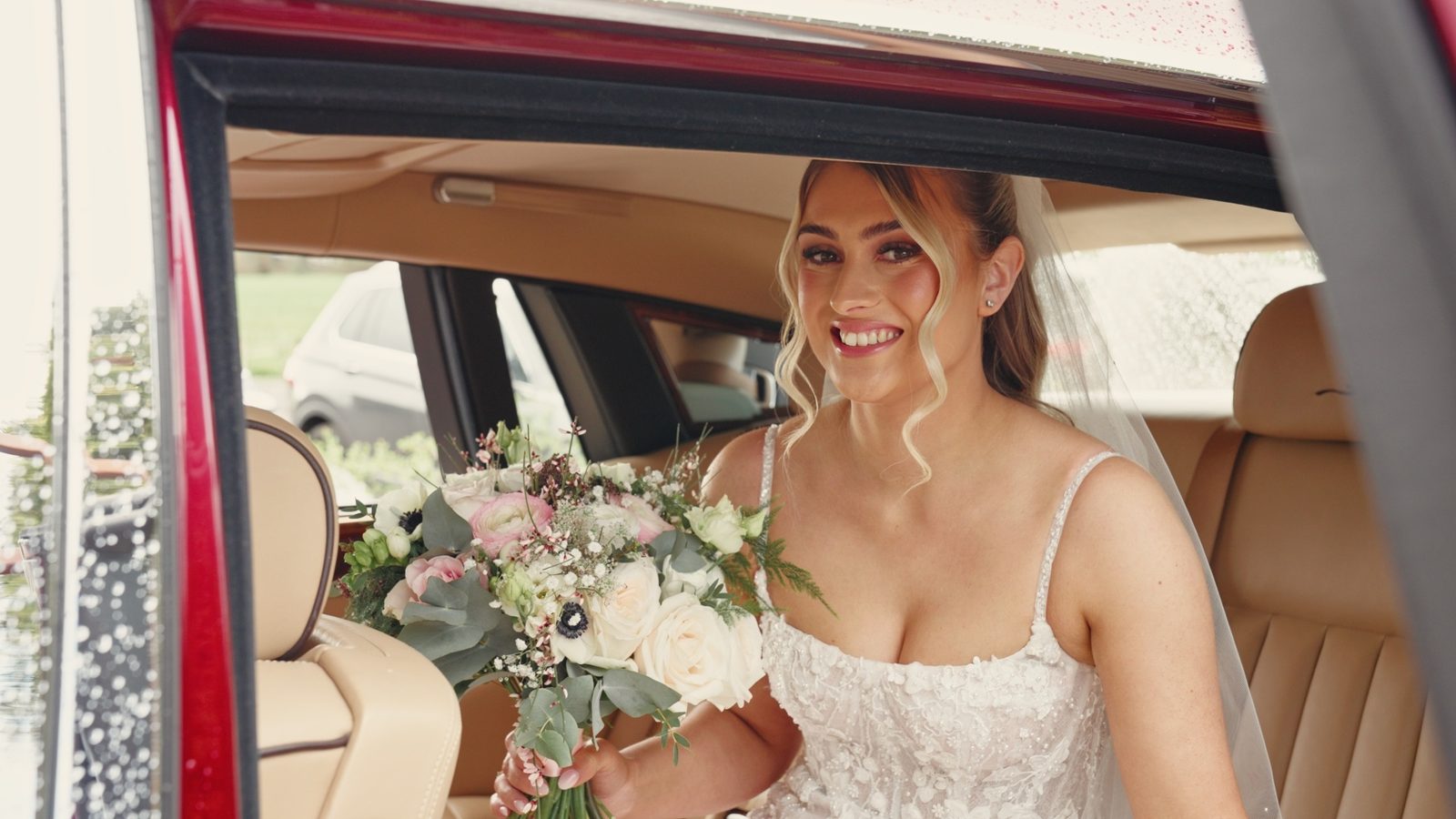 A smiling bride holding her bouquet in the back of the wedding car