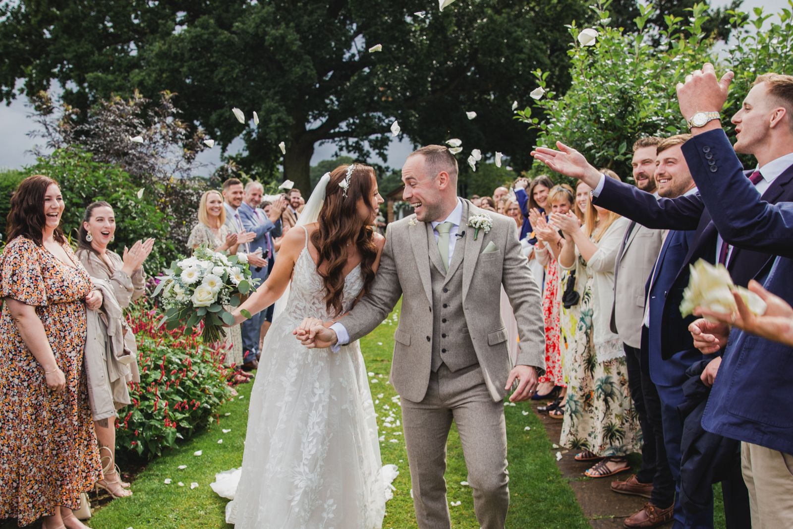 A bride and groom laughing as guests throw petals over them