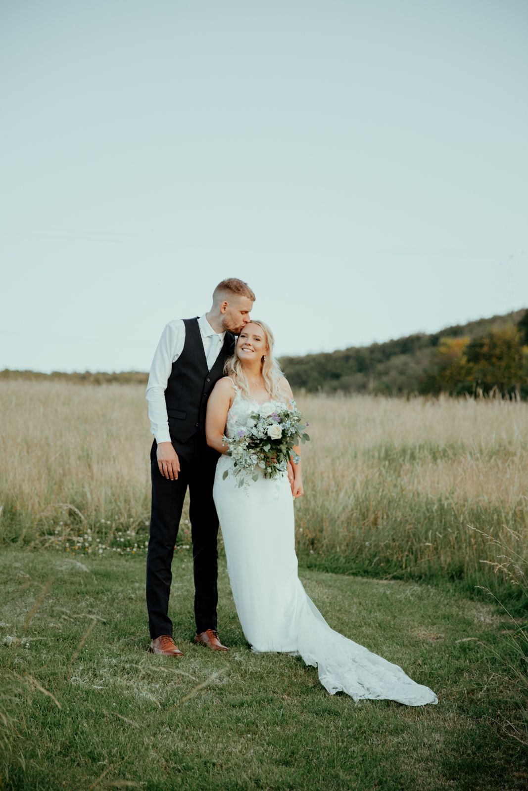 The groom kissing the bride's forehead in a meadow