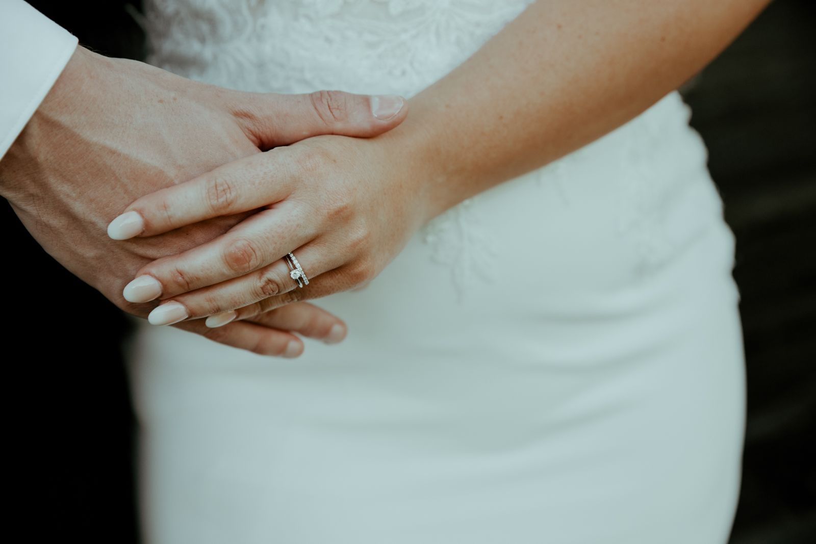 A bride's hand with her rings resting on the groom's